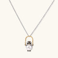 Whimsical penguin pendant holding a white pearl on a gold swing, rhodium-plated silver chain on cream background.